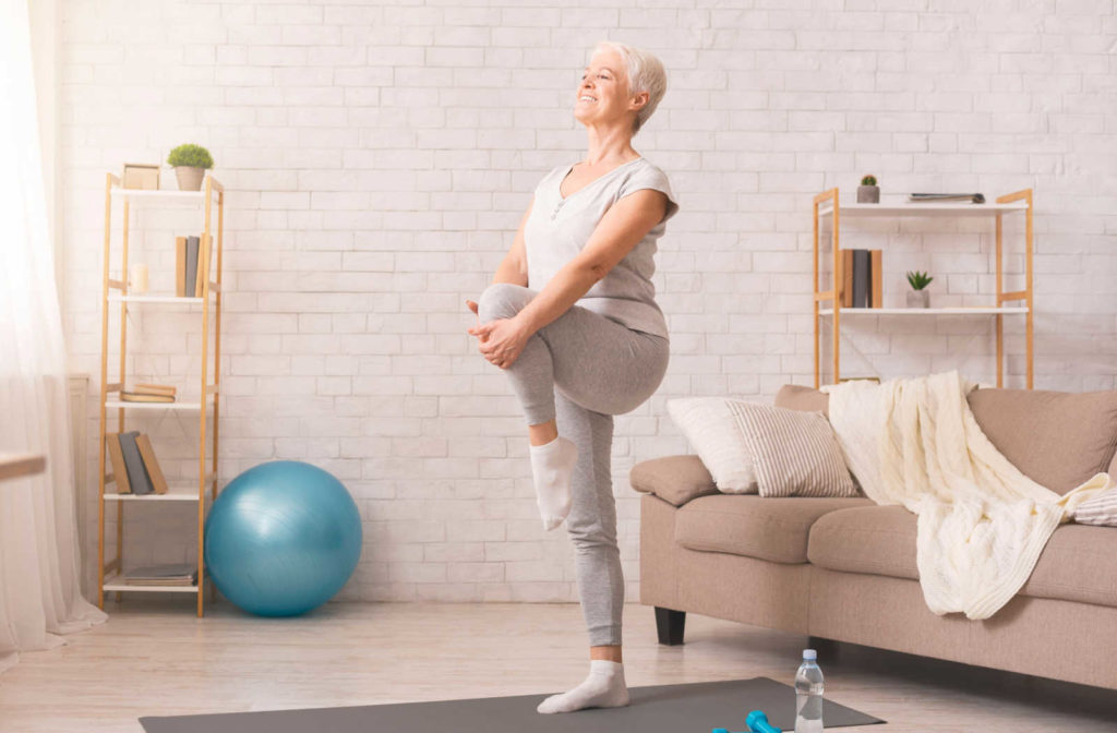 A senior woman does a balance exercise at home.