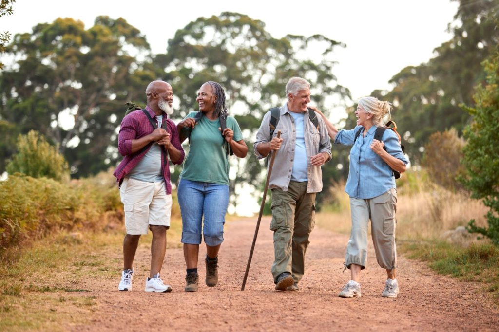 A group of 4 smiling seniors enjoying a day hike together.
