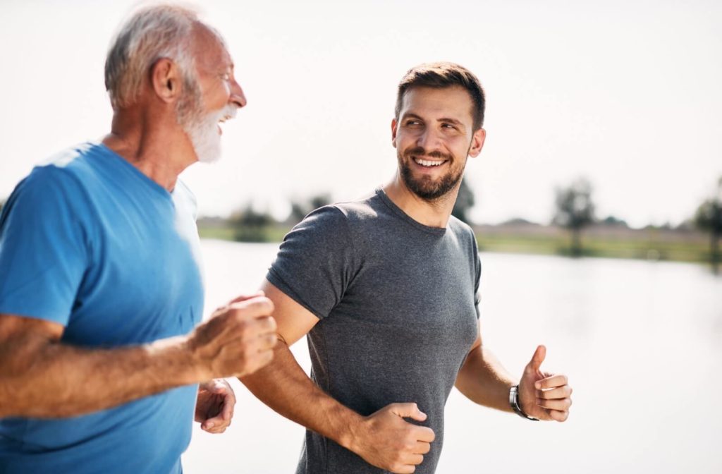 A smiling older parent and adult son jogging together outdoors.