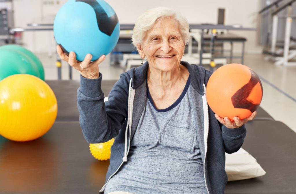 Senior sitting on a bench, smiling, holding an orange ball in one hand and a blue ball in the other.