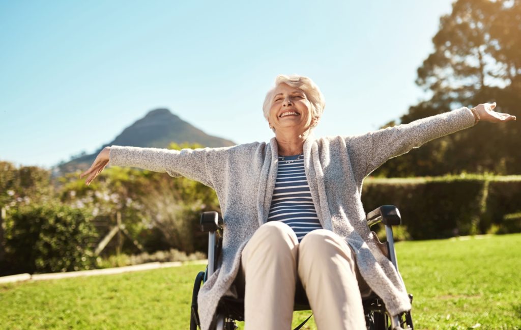 A senior sits outside. The warm sun hits their face and they outstretch their arms with joy and reassurance.