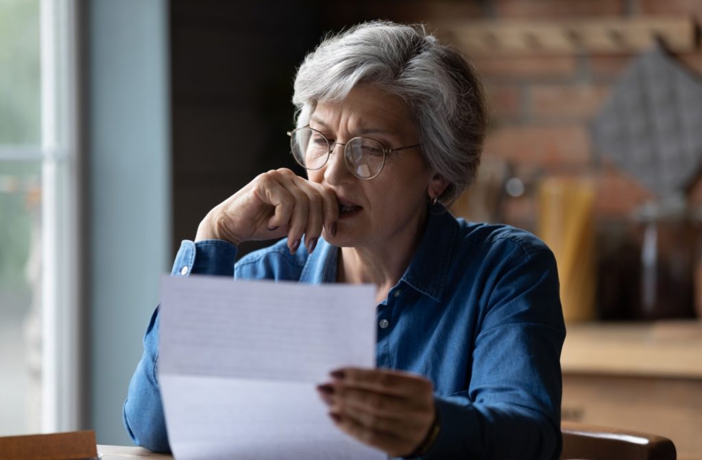 An older woman reading a document with a concerned expression while sitting at a table.