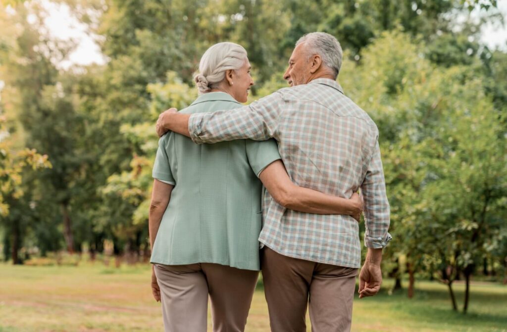 A shot from behind of a healthy older couple walking through a park and smiling at one another.