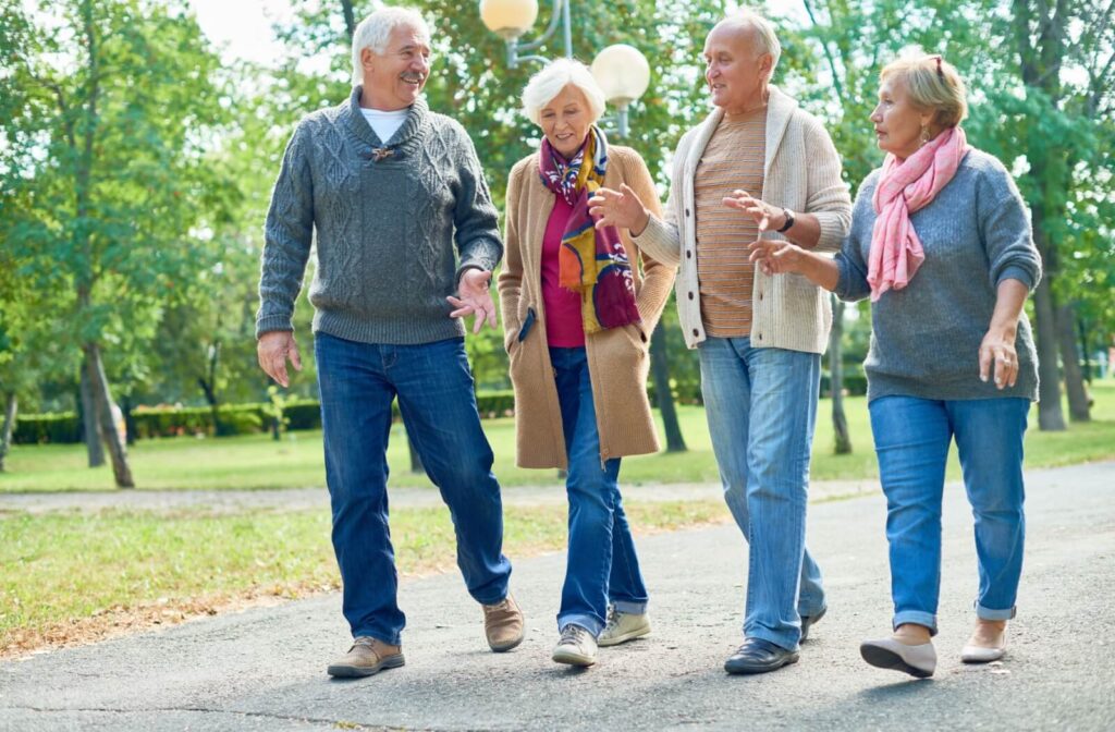 A group of senior friends enjoy lively conversation while walking in a park near their senior living home for cardio exercise