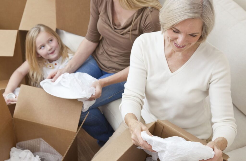 Older adult unpacks dishes with family while moving surrounded by cardboard boxes downsizing with support and care