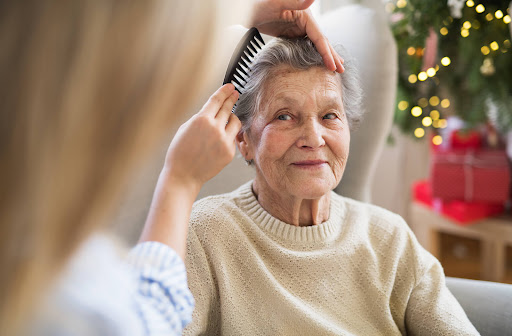 A woman in the foreground with her back to the camera combs an elderly woman's hair.