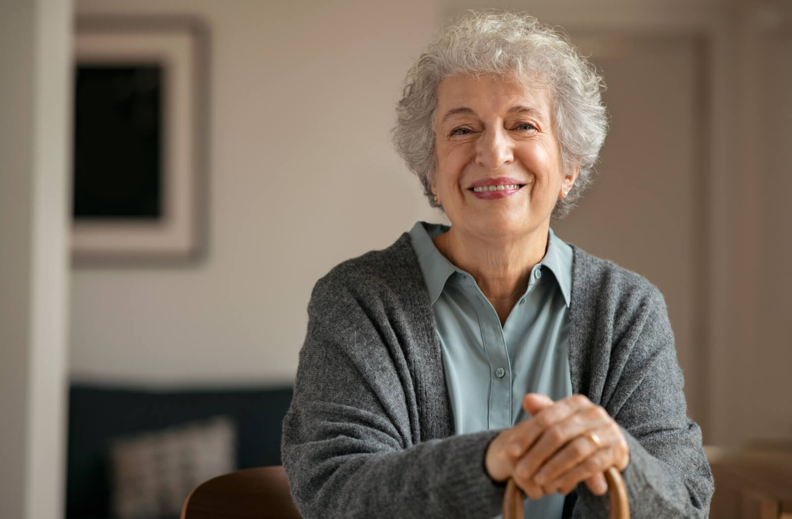 A senior woman with short gray hair holding a cane looking directly and smiling.