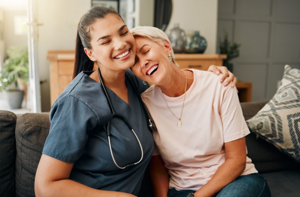 An older adult laughs while leaning their head on their nurse’s shoulder, grateful for the support in respite care.