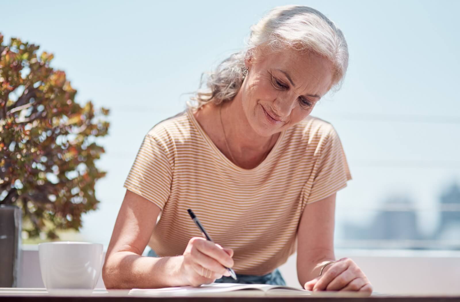 An older adult sitting beside a window in the morning, journaling as they get ready for the day.