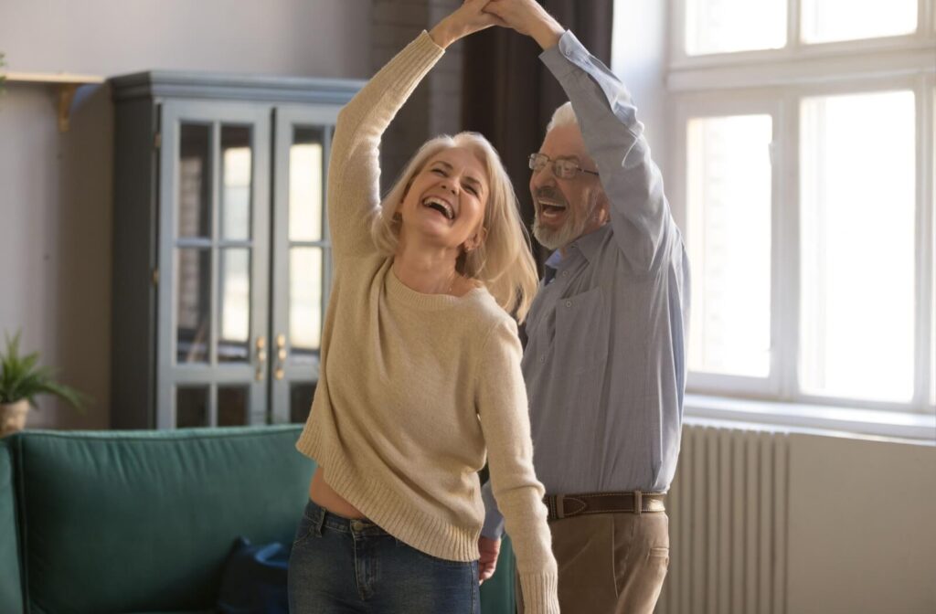 An older couple dancing in their living room in senior living, laughing and having fun together.