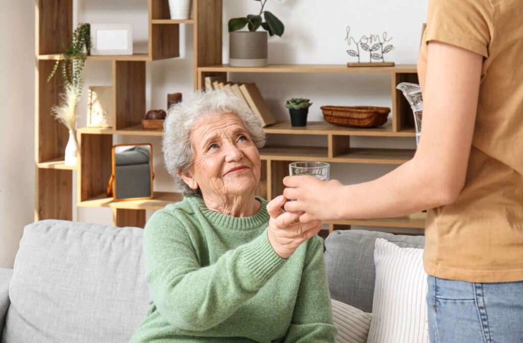 An adult child handing a grateful older adult a glass of water in senior living.