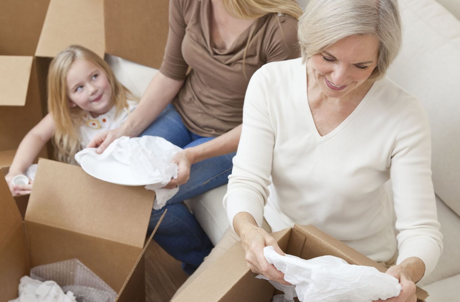 Older adult unpacks dishes with family while moving surrounded by cardboard boxes downsizing with support and care
